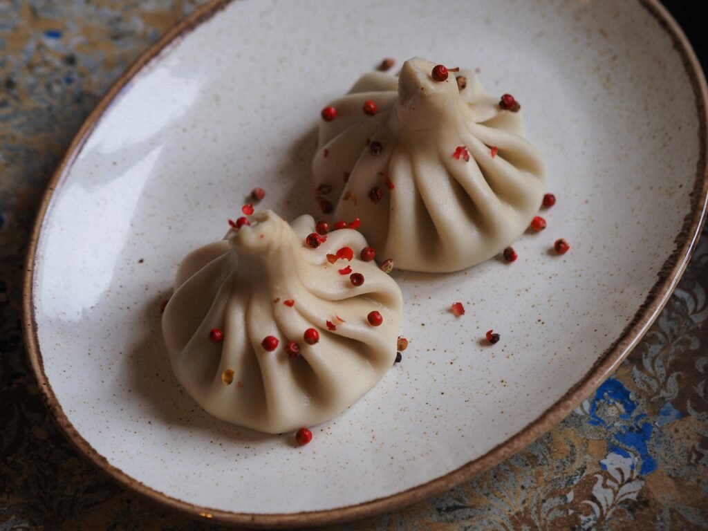 Two Georgian khinkali dumplings with pepper corns on a rustic plate.